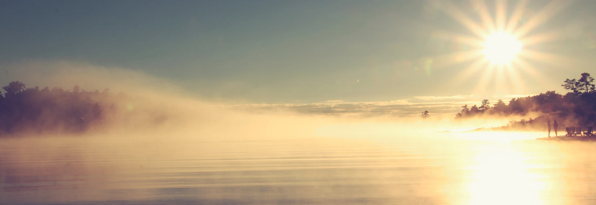 Nebel und Tau über einem See verflüchtigen sich beim Sonnenaufgang